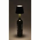 A wine bottle lamp with a black lampshade glowing in the dark.