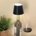 Lamp on wine bottle base next to a wine glass and plant.