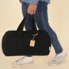 Person in jeans and sneakers carrying a black duffel bag.