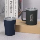 Two travel mugs on a counter beside stacked books.