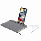 Phone docked on a gray notebook with a pen nearby.