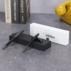 Two pens on black and white boxes, with books and a yellow object in the background.