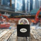 Close-up of a padlock on a wooden surface, with a blurred construction site in the background.