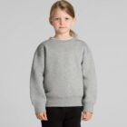 Child wearing a gray sweatshirt and black pants, standing against a gray background.