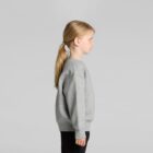 Child in profile view wearing a gray sweatshirt and black pants against a gray background.