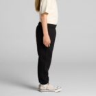 Child in a white shirt and black pants standing sideways against a gray background.