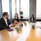 Three people having a meeting at a conference table with laptops and coffee cups.