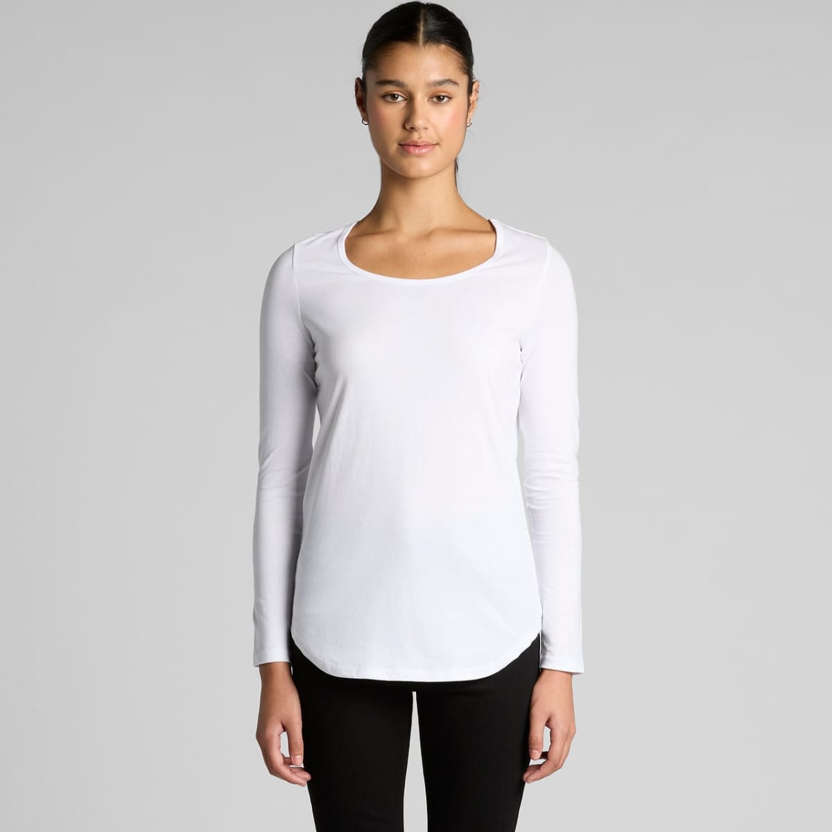 Person in a white long-sleeve shirt and black pants standing against a gray background.