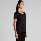 Woman in a plain black t-shirt and black pants standing against a gray background.