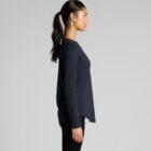 Woman in a black long-sleeve top and ponytail, standing sideways against a gray background.