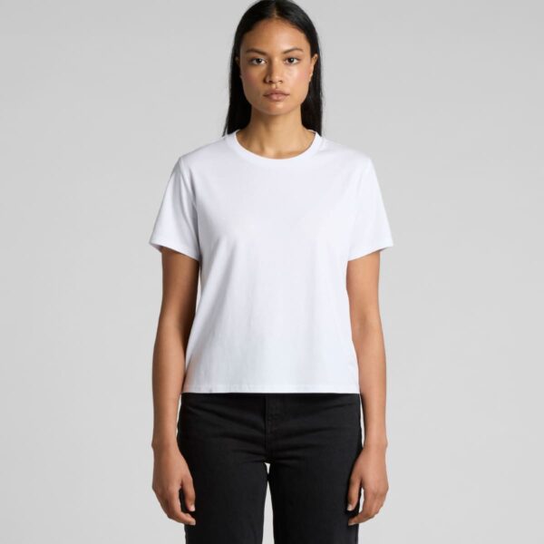Woman standing in a plain white T-shirt and black pants against a gray background.