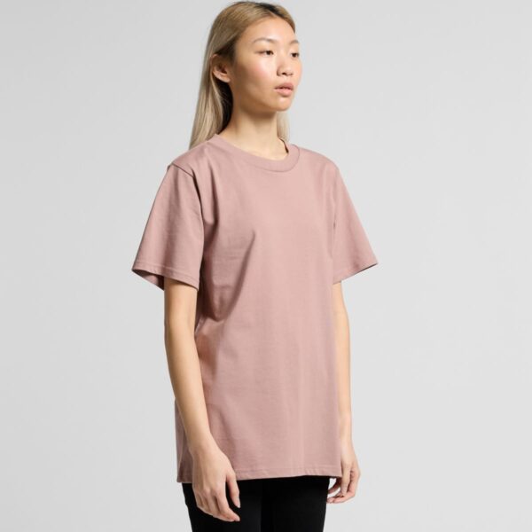 A person wearing a plain mauve t-shirt and black pants stands against a gray background.