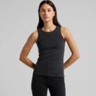Woman in black sleeveless top and black jeans standing against a plain gray background.