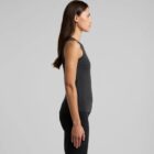 Woman in a black tank top and pants standing in profile against a gray background.