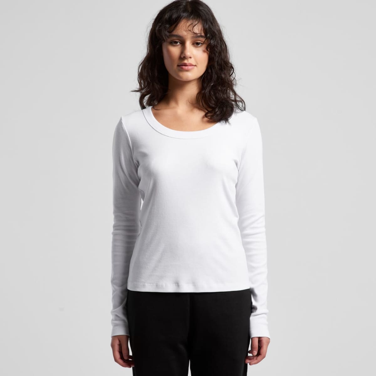 Woman with wavy hair wears a long-sleeve white shirt and black pants, facing forward.