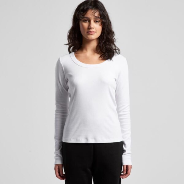 Woman in a white long-sleeve shirt and black pants standing against a gray background.