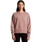 Woman in a mauve sweatshirt and black pants standing against a plain white background.