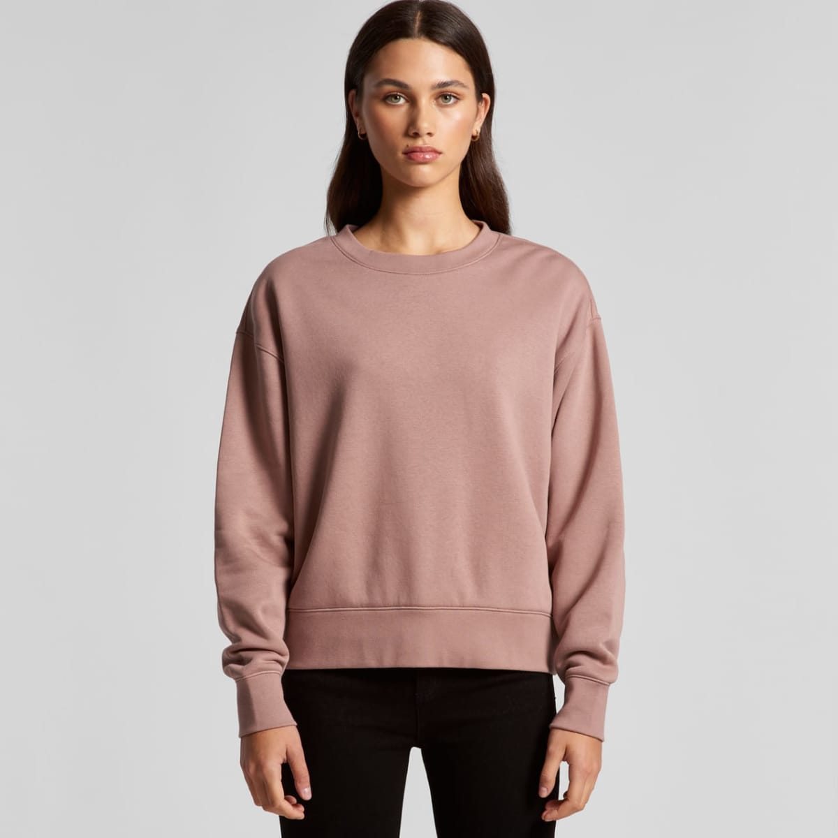 Woman in a mauve sweatshirt and black pants standing against a plain gray background.