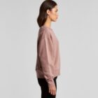 Woman in a mauve sweatshirt and black pants standing in profile against a plain background.