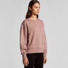 Woman in a mauve sweatshirt and black pants standing against a plain background.
