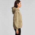 A woman in a tan hoodie and black pants stands in profile against a plain background.