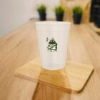 A translucent cup with a green flame logo on a wooden table.