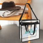 A clear tote bag hangs on a wooden chair with a hat and sweater on the seat.