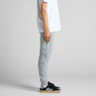 Person in white shirt, gray joggers, and sneakers, standing in profile against a plain backdrop.