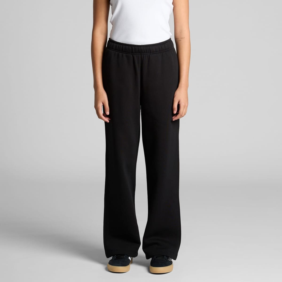 Person in a white top and black pants, standing against a plain gray background.