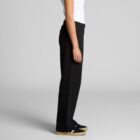 Person in black pants and black sneakers standing in profile against a plain gray background.