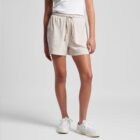 Person in white top, beige shorts, and white sneakers against a plain background.