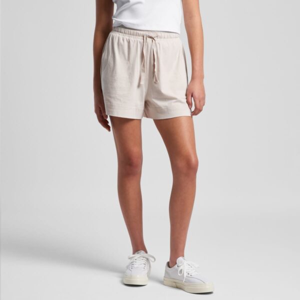 Person in a white top, beige shorts, and white sneakers against a plain background.