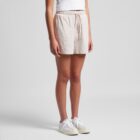 Person wearing a white shirt, beige shorts, and white sneakers stands against a plain background.