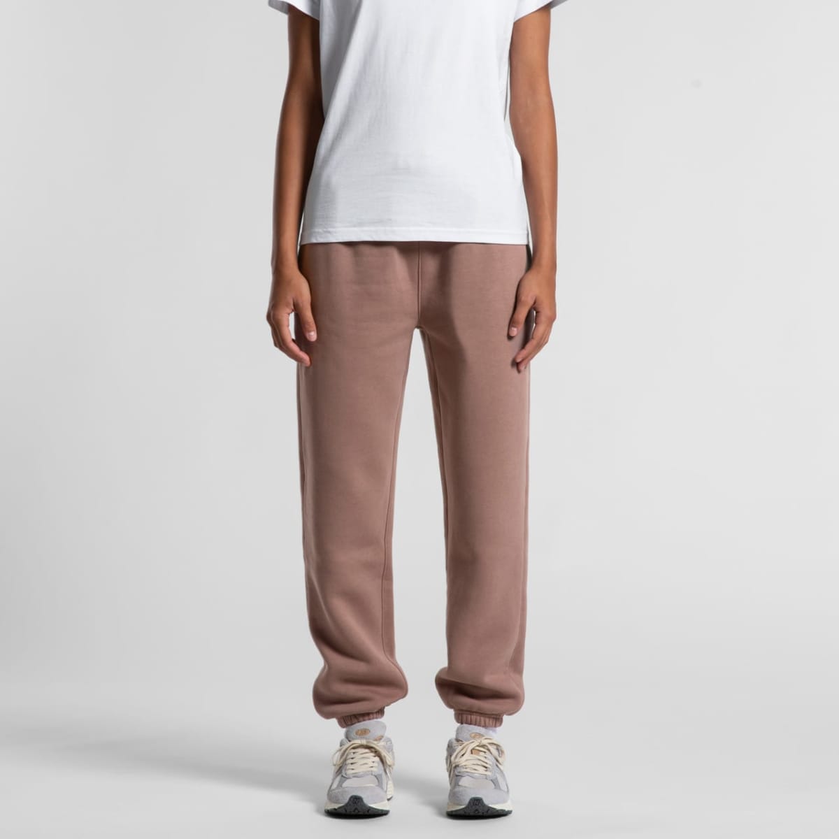 Person wearing a white shirt, brown sweatpants, and white sneakers, standing against a white background.
