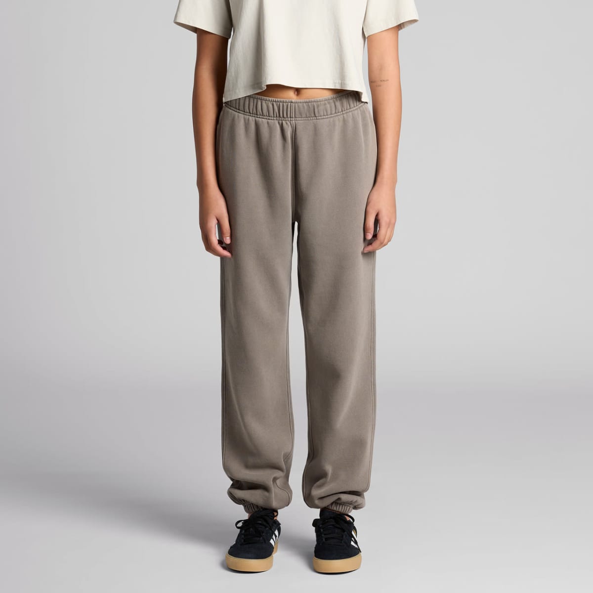 Person in beige crop top and gray sweatpants standing against a plain background.