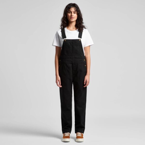 Person standing, wearing black overalls, white t-shirt, and brown shoes against a plain background.