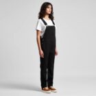 Person in black overalls, white t-shirt, and brown shoes standing against a plain background.