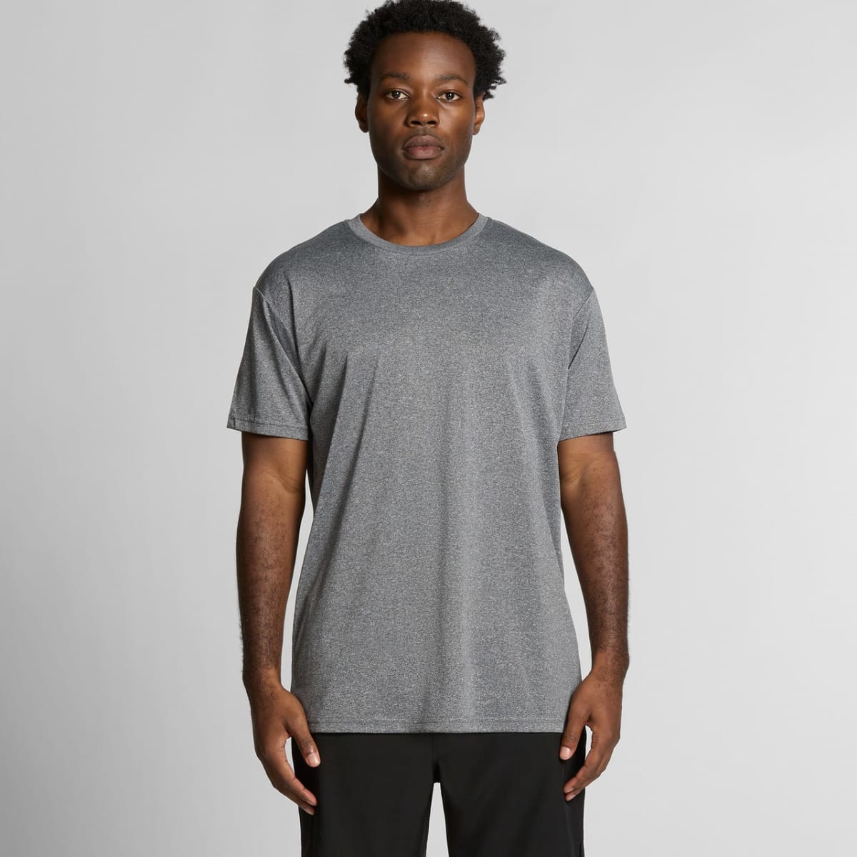Man standing in a gray t-shirt and black pants against a plain light background.