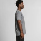 Man in a gray T-shirt and black pants standing in profile against a plain background.