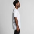 Man standing in profile wearing a light gray T-shirt and black pants against a plain background.
