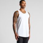 Man wearing a white tank top and black pants, standing against a plain background.