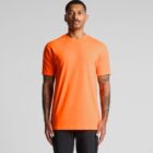 Man wearing a bright orange t-shirt and black pants, standing against a plain background.