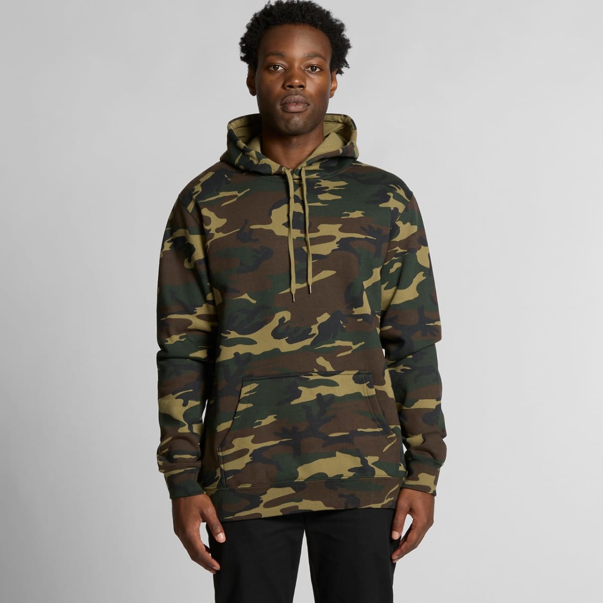 Man wearing a green camouflage hoodie and black pants standing against a plain background.