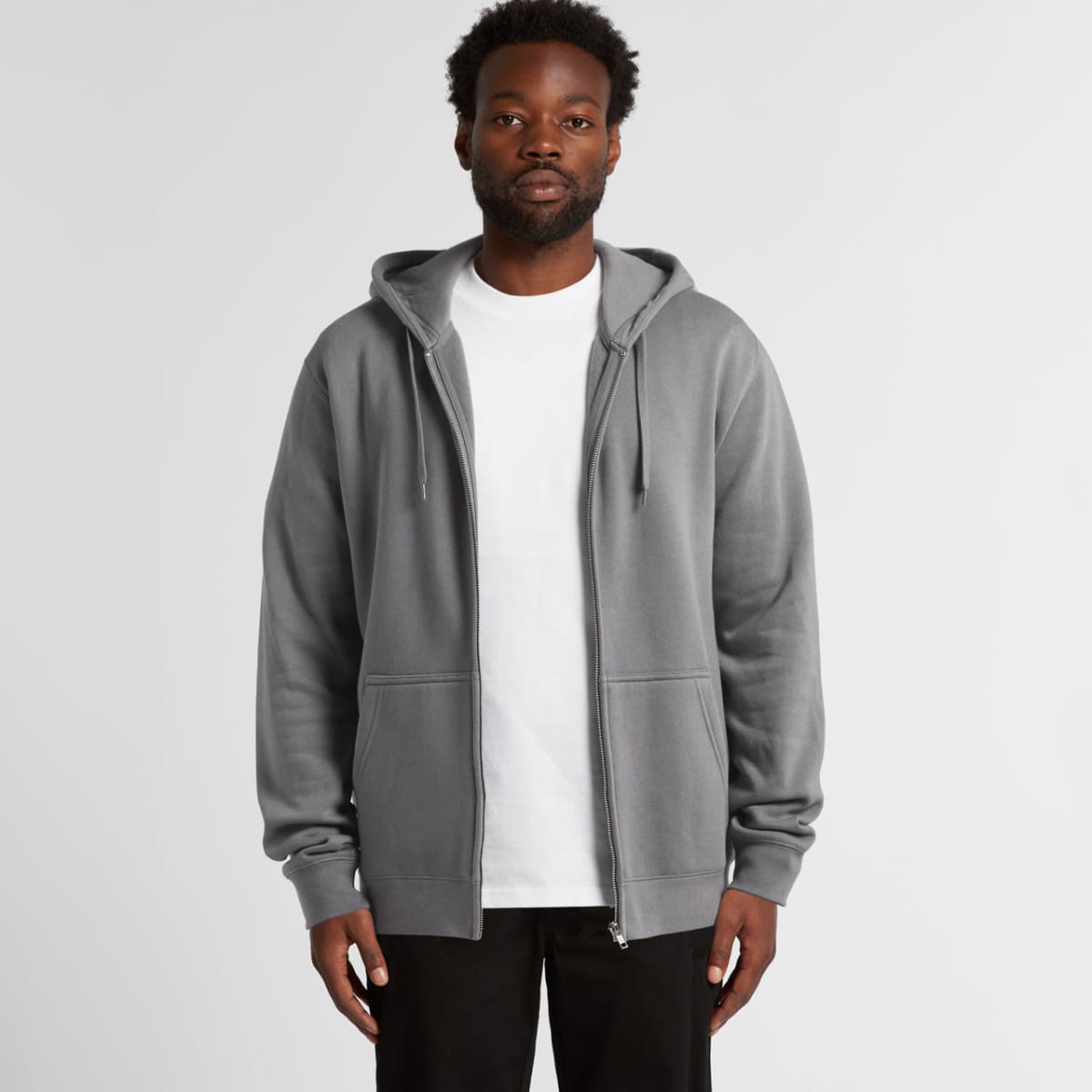 Man wearing a gray zip-up hoodie over a white t-shirt, standing against a plain background.
