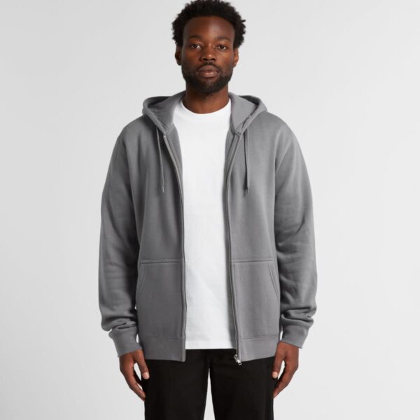 Man wearing a gray zip-up hoodie over a white t-shirt, standing against a plain background.