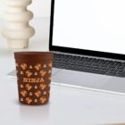 A brown Ninja cup on a desk next to an open laptop.