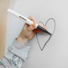 Child drawing a heart on a whiteboard with a black marker.