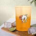 Yellow cup with cartoon dog peeing on post, on table with ice cubes and lime wedge.