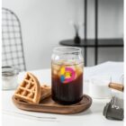 A glass of iced coffee with waffles on a wooden tray, on a white table.