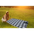 Woman in hat spreading a plaid blanket on grass during sunset.